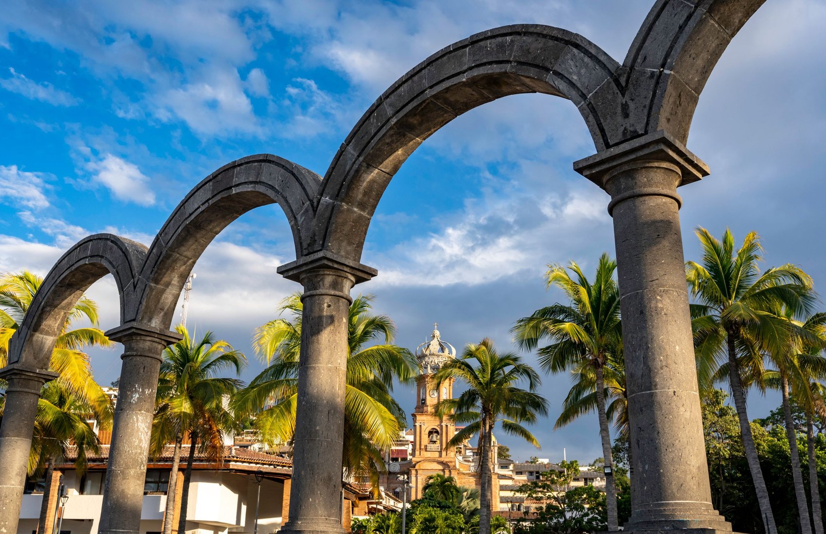 Los Arcos del Malecón de Puerto Vallarta con palmeras y la torre de la parroquia de Guadalupe al fondo