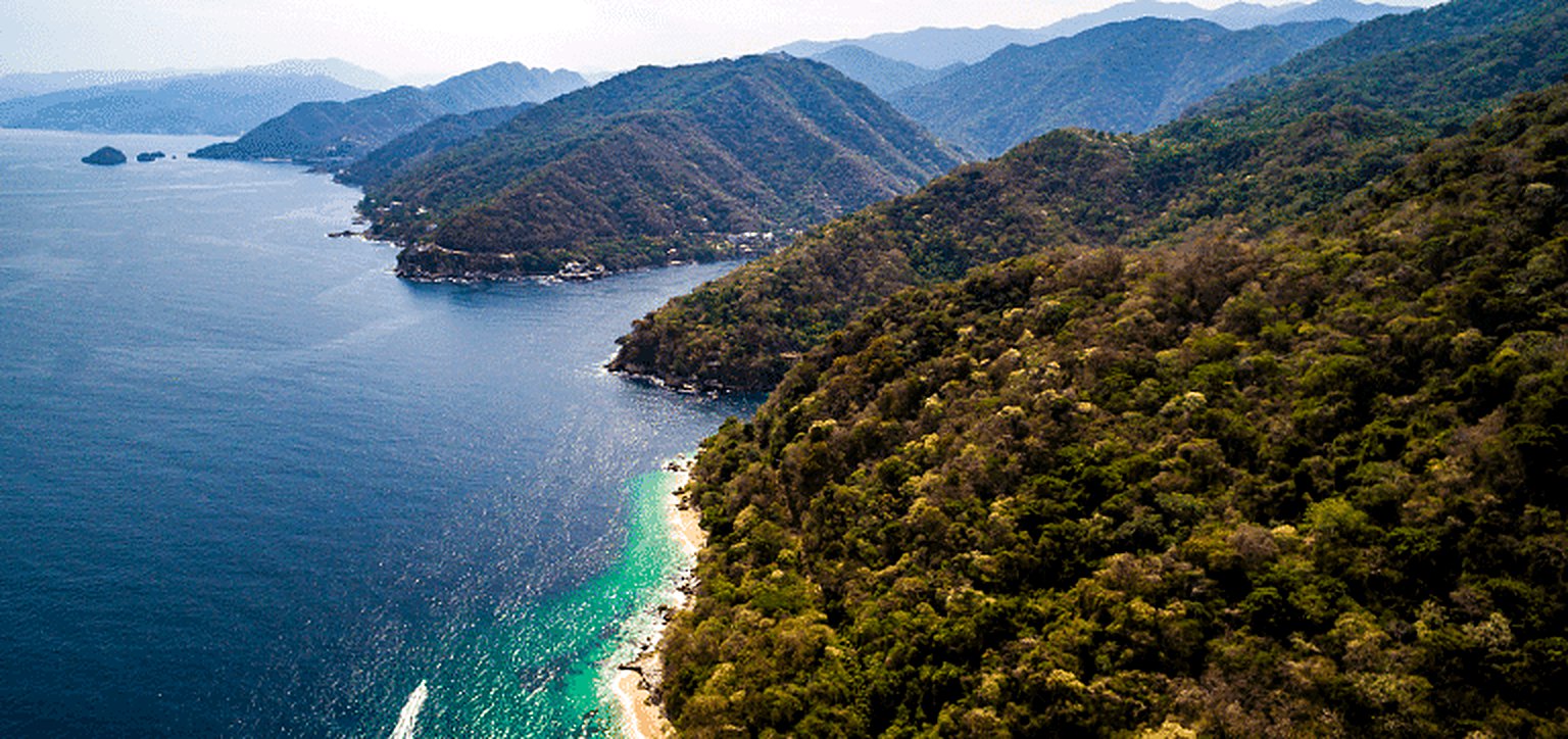 Vista aérea de la costa de Bahía de Banderas: montañas cubiertas de selva que caen al Pacífico y una playa de agua turquesa